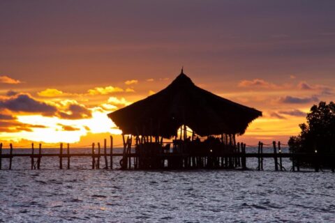 Het paviljoen met rieten dak van Fundu Lagoon, op palen aan het eind van de steiger, bij zonsondergang