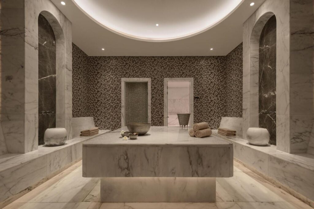 Een ruimte in de spa van het JAZ Elite Riviera, bekleed met marmer, met een brede stenen tafel in het midden