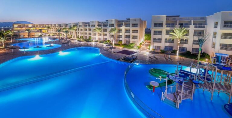 De verlichte zwembaden van het JAZ Soma Beach bij het vallen van de avond, tussen de gebouwen en de palmbomen