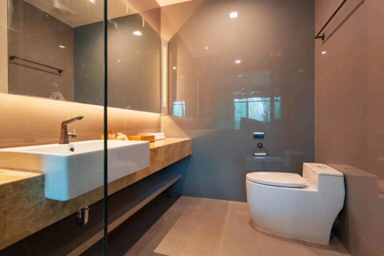 Een badkamer met een waskom op een marmeren blad, een verlichte spiegel en een toilet