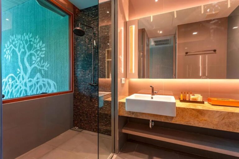 Een douche achter een glazen wand, bij een raam met een boommotief