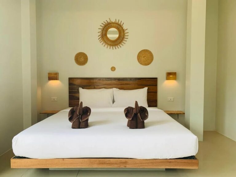 Een tweepersoonsbed met een houten hoofdeinde, olifanten van handdoeken en een rotan zonnespiegel