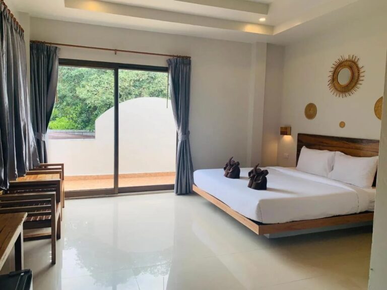 Een kamer met een tweepersoonsbed, een glazen schuifpui naar een balkon en houten fauteuils