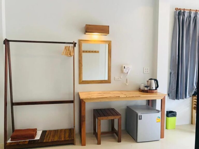 Een houten kledingrek, een spiegel en een bureau met een waterkoker boven een kleine koelkast