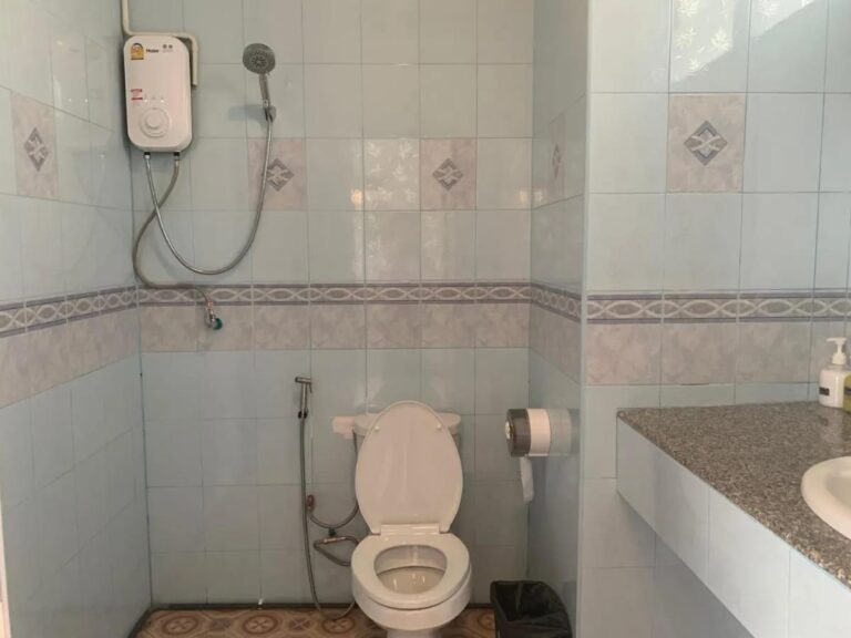 Een betegelde badkamer met een douche met boiler, een toilet en een wastafel