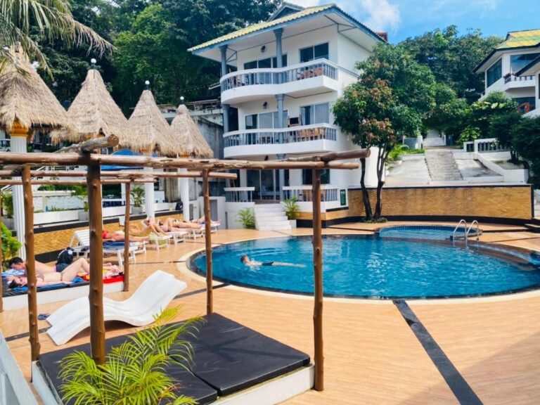 Het zwembad van het Koh Tao Heritage, met ligstoelen en strooien parasols, voor een gebouw met balkons