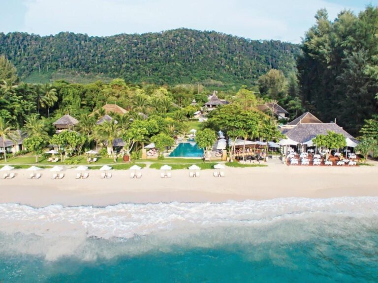 Het Layana Resort gezien vanaf zee, met het strand, de witte parasols, het zwembad en de daken onder de palmbomen