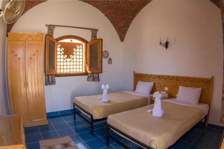 Een kamer met twee bedden onder een bakstenen gewelf, met een kast en houten luiken