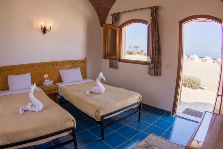 Een kamer met twee bedden onder een bakstenen gewelf, met de deur open naar het zand