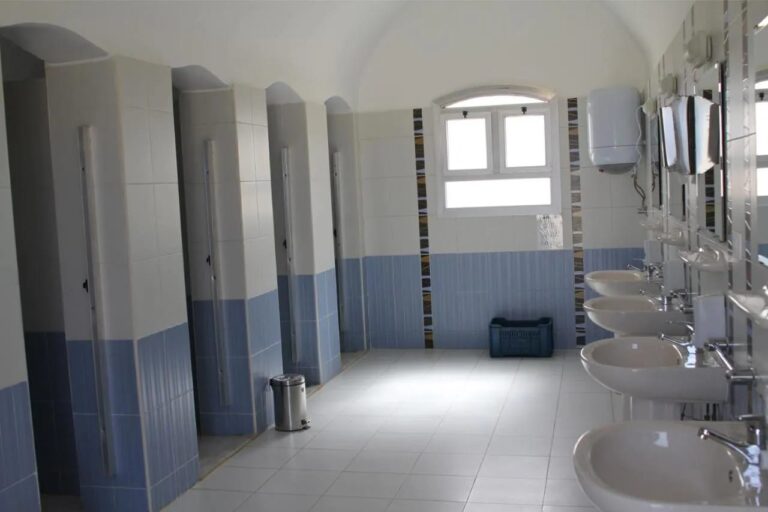 Een sanitairblok met cabines op een rij en een reeks wastafels