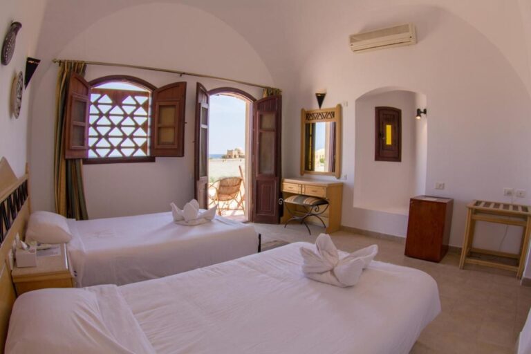 Een kamer met twee bedden onder een wit gewelf, met de deur open naar een terras en de zee