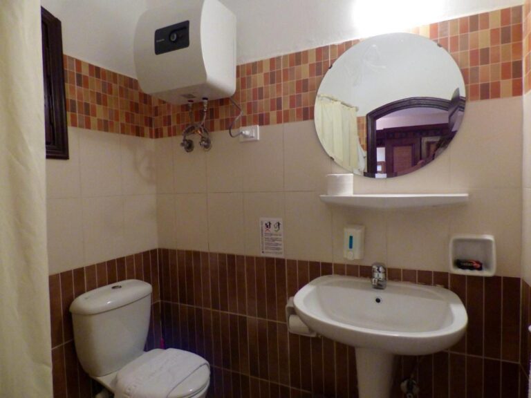 Een badkamer met wastafel, toilet, ronde spiegel en boiler