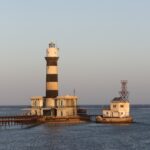 De vuurtoren van Daedalus, een zwart-wit gestreepte toren op het rif, met zijn gebouwen en metalen steiger, bij zonsondergang
