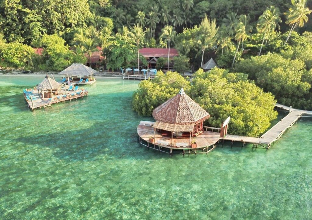 Luchtfoto van de Raja Ampat Dive Lodge, met de steigers op palen en de rode daken onder de palmbomen