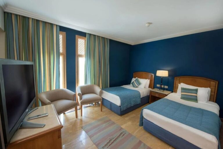 Een kamer met twee bedden en blauwe muren, met twee fauteuils voor de ramen