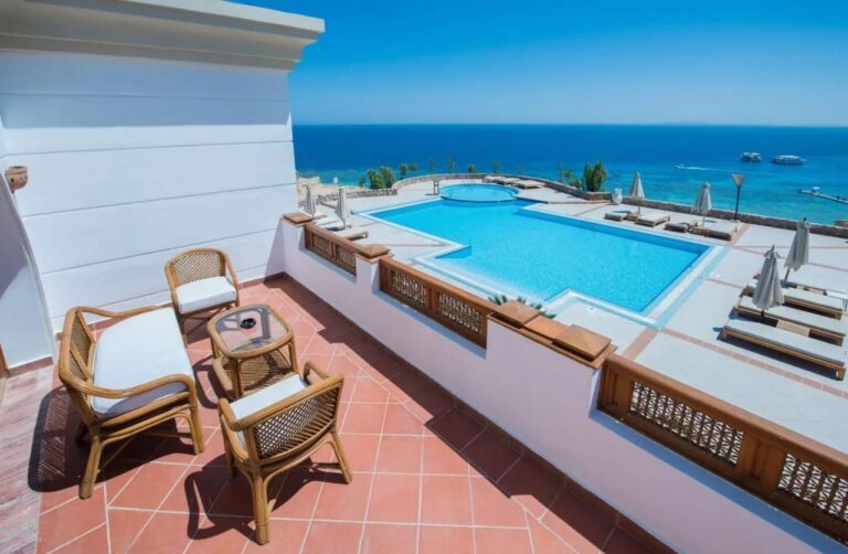 Een terras met rotan meubels boven een groot zwembad en de Rode Zee, in het Reef Oasis Beach Resort