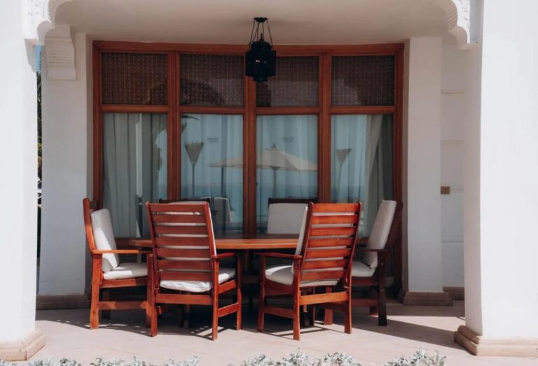 Een overdekt terras met een houten tafel en zes stoelen, onder een lantaarn