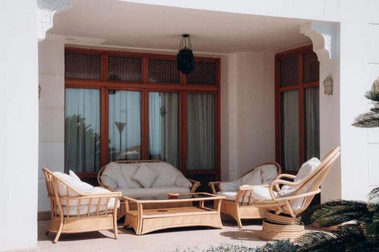 Een overdekt terras met een rotan bank en fauteuils