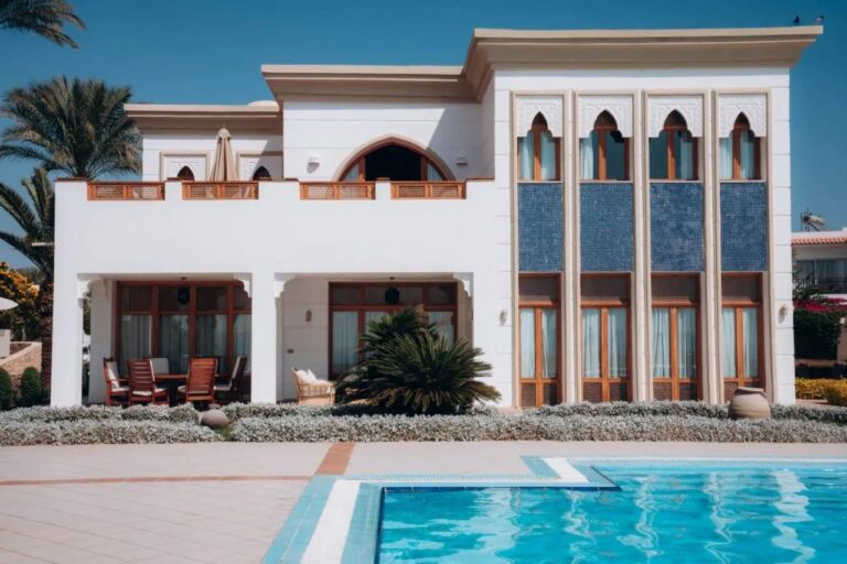 Een wit gebouw van het Reef Oasis Beach Resort, met boogramen en blauwe mozaïekpanelen, voor een zwembad