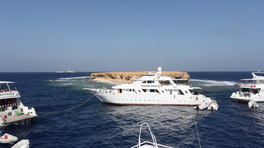 Drie liveaboards afgemeerd voor het vlakke eilandje Small Brother, met de vuurtoren van Big Brother aan de horizon