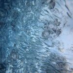Een dichte school zilveren sardines scheert over een heel lichte zandbodem met donkere rotsen, de massa vissen dichter naar links, in het blauw.