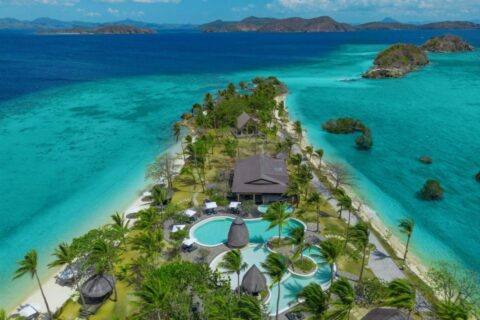 Luchtfoto van het Two Seasons Coron, met zijn zwembaden en palmbomen op een smalle strook land tussen twee stranden
