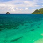 Luchtfoto van het lange strand van Le Diamant langs turquoise water, met Diamond Rock voor de kust en rechts de Morne Larcher, een groene heuvel