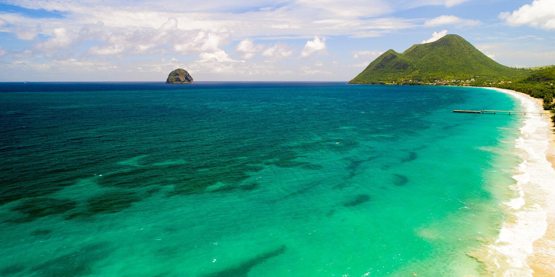Luchtfoto van het lange strand van Le Diamant langs turquoise water, met Diamond Rock voor de kust en rechts de Morne Larcher, een groene heuvel